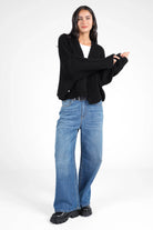Frau trägt schwarzen ALIXA Cropped Strickcardigan im Oversize-Look mit Schalkragen und gerippten Abschlüssen zu blauen Jeans