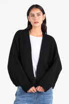 Damen trägt schwarzen ALIXA Cropped Strickcardigan mit Schalkragen und Oversize-Fit zu weißem Shirt und Jeans