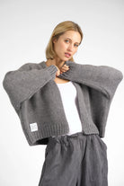 Woman wearing grey ALIXA Cropped Strickcardigan with loose fit and ribbed cuffs over a white top.