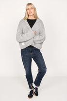 Woman wearing grey ALIXA Cropped Strickcardigan with oversized fit, shawl collar, and ribbed cuffs paired with dark jeans and black sneakers
