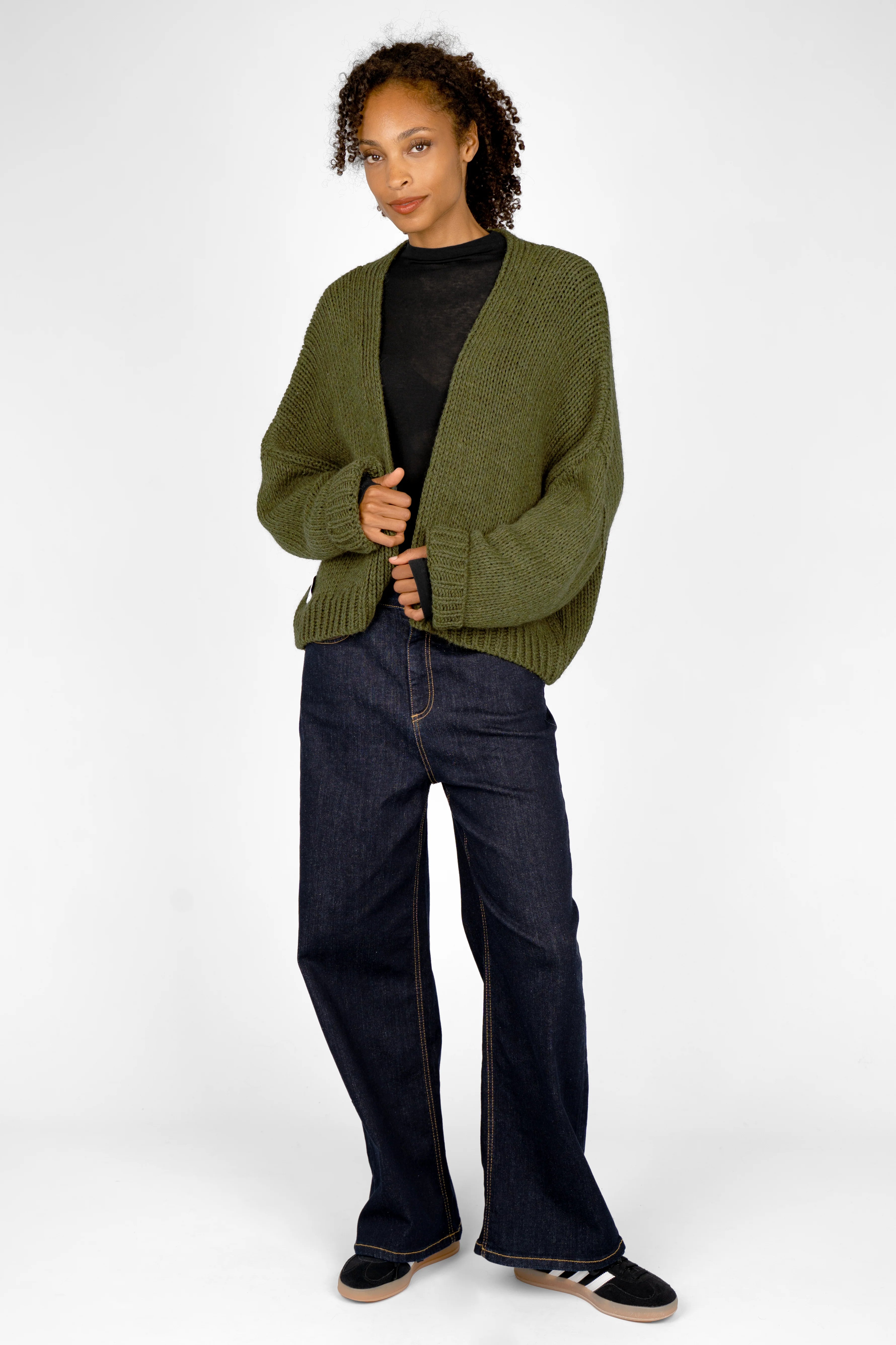 Woman wearing olive green ALIXA Cropped Strickcardigan with loose fit and wide cuffs over black top and dark jeans