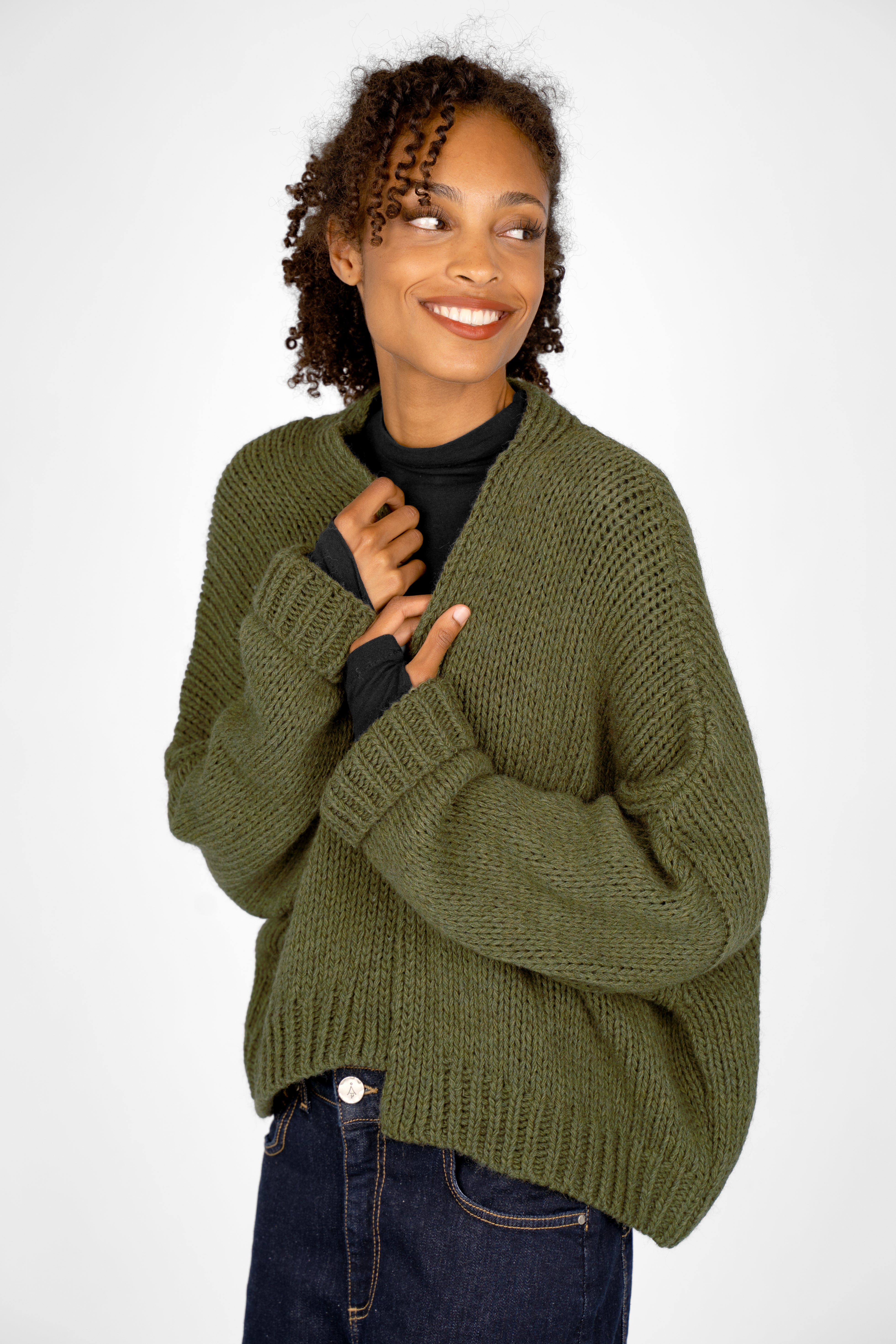 Woman wearing olive green ALIXA Cropped Strickcardigan with shawl collar and loose fit over black top.