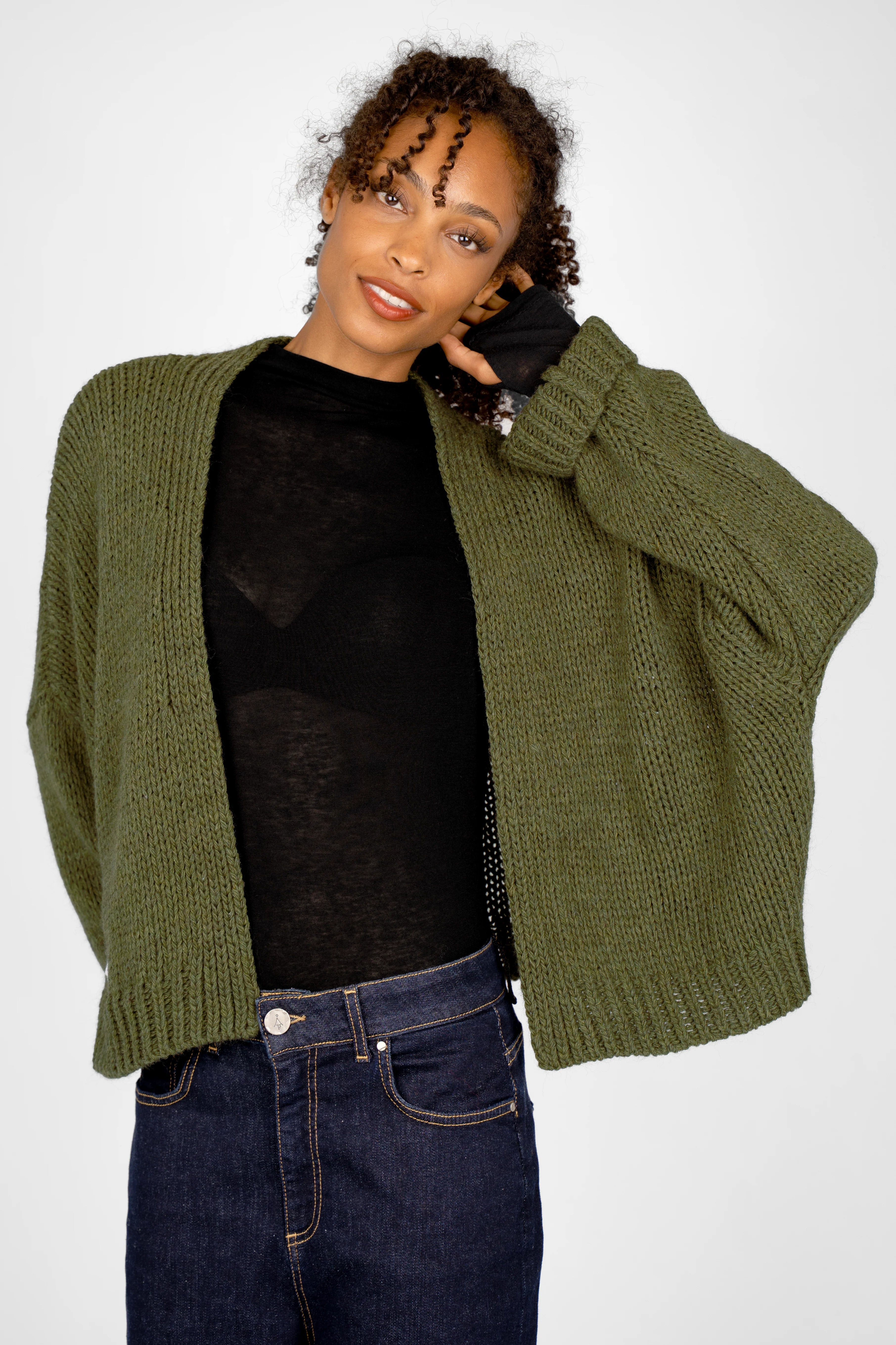 Woman wearing olive green ALIXA Cropped Strickcardigan with loose fit and ribbed cuffs over black top and jeans