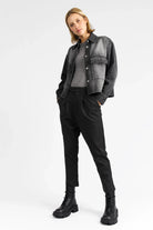 Damenmodell trägt schwarze AMAKU Revive Hemdjacke aus strukturierter Baumwolle mit Knopfleiste und Brusttaschen im lässigen Denim-Look.