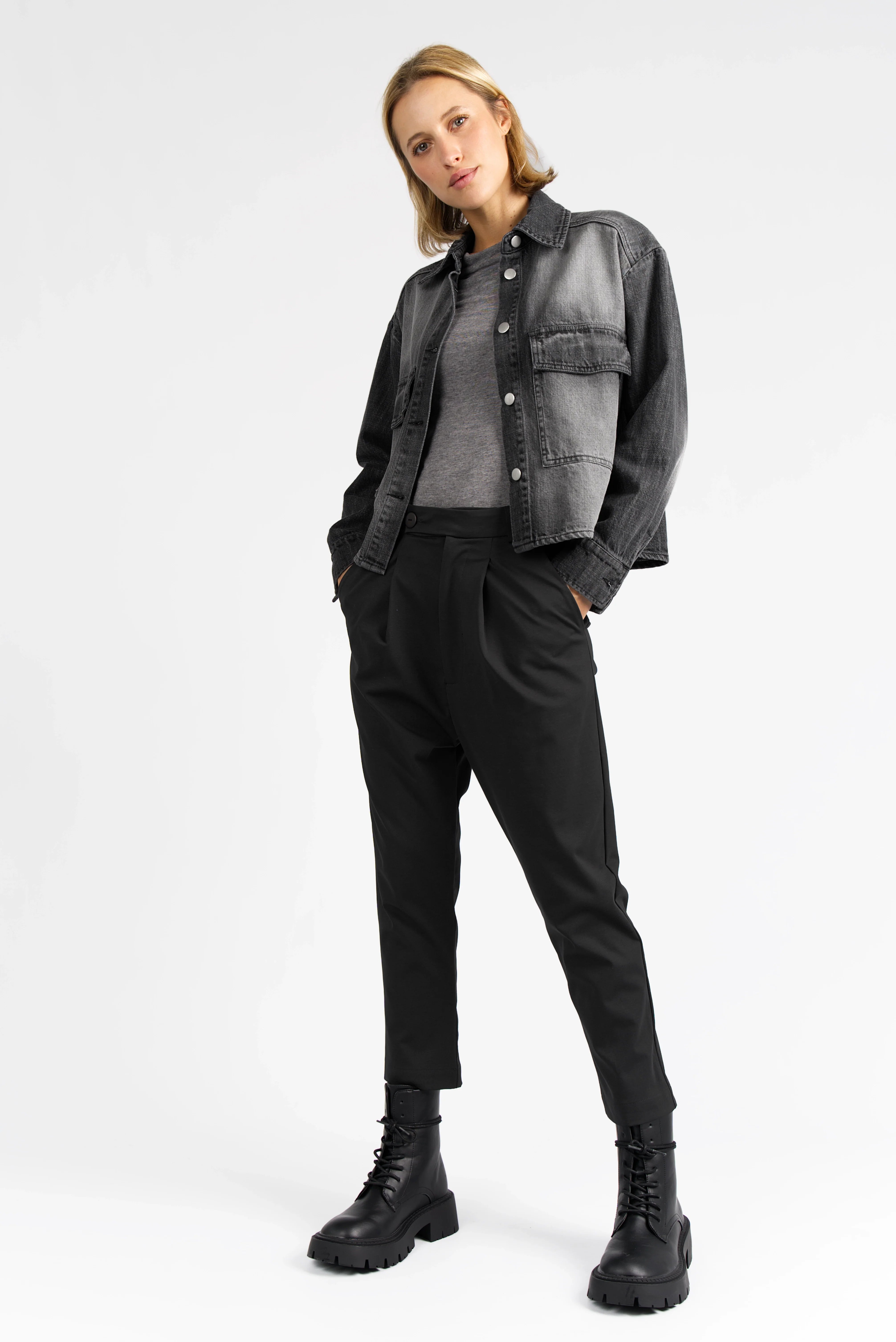 Damenmodell trägt schwarze AMAKU Revive Hemdjacke aus strukturierter Baumwolle mit Knopfleiste und Brusttaschen im lässigen Denim-Look.