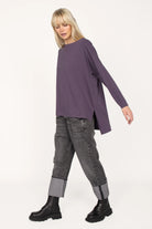 AMALEA Relaxed Fit purple long sleeve top with boat neckline, dropped shoulders, side slits, and extended back hem worn with cuffed gray jeans and black boots