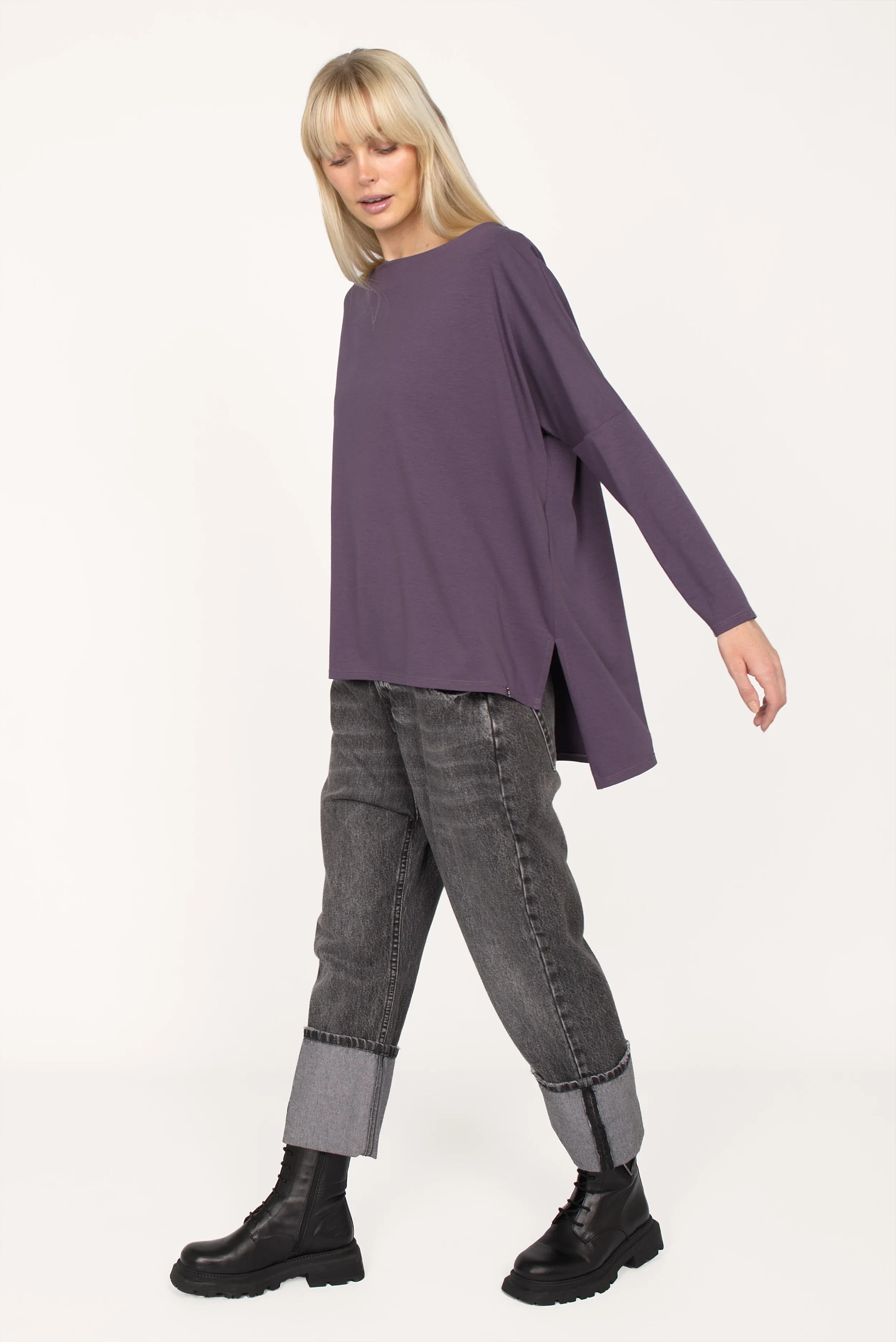 AMALEA Relaxed Fit purple long sleeve top with boat neckline, dropped shoulders, side slits, and extended back hem worn with cuffed gray jeans and black boots