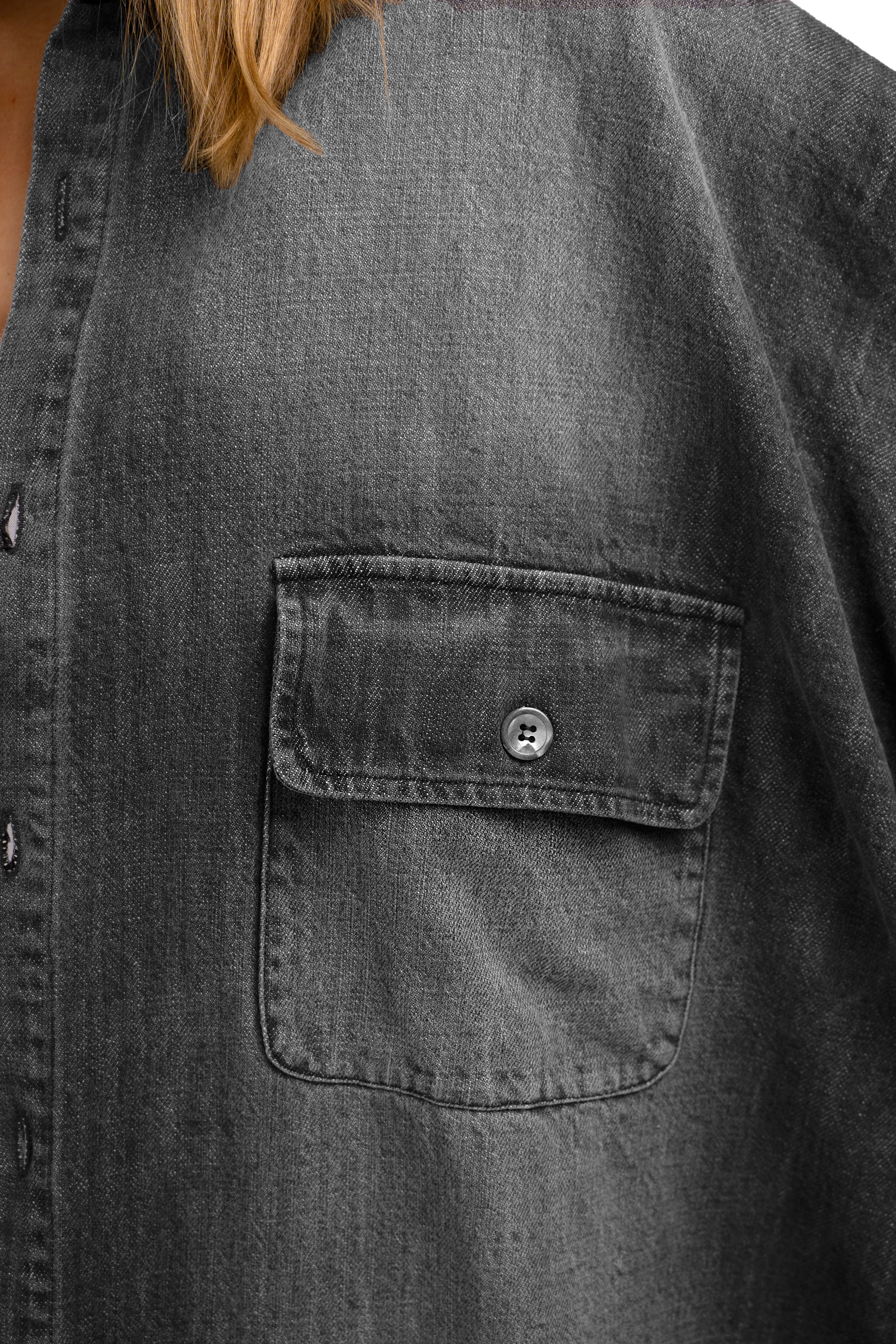 Close-up of gray ANEA Oversized Hemdjacke with buttoned chest pocket and textured cotton fabric.