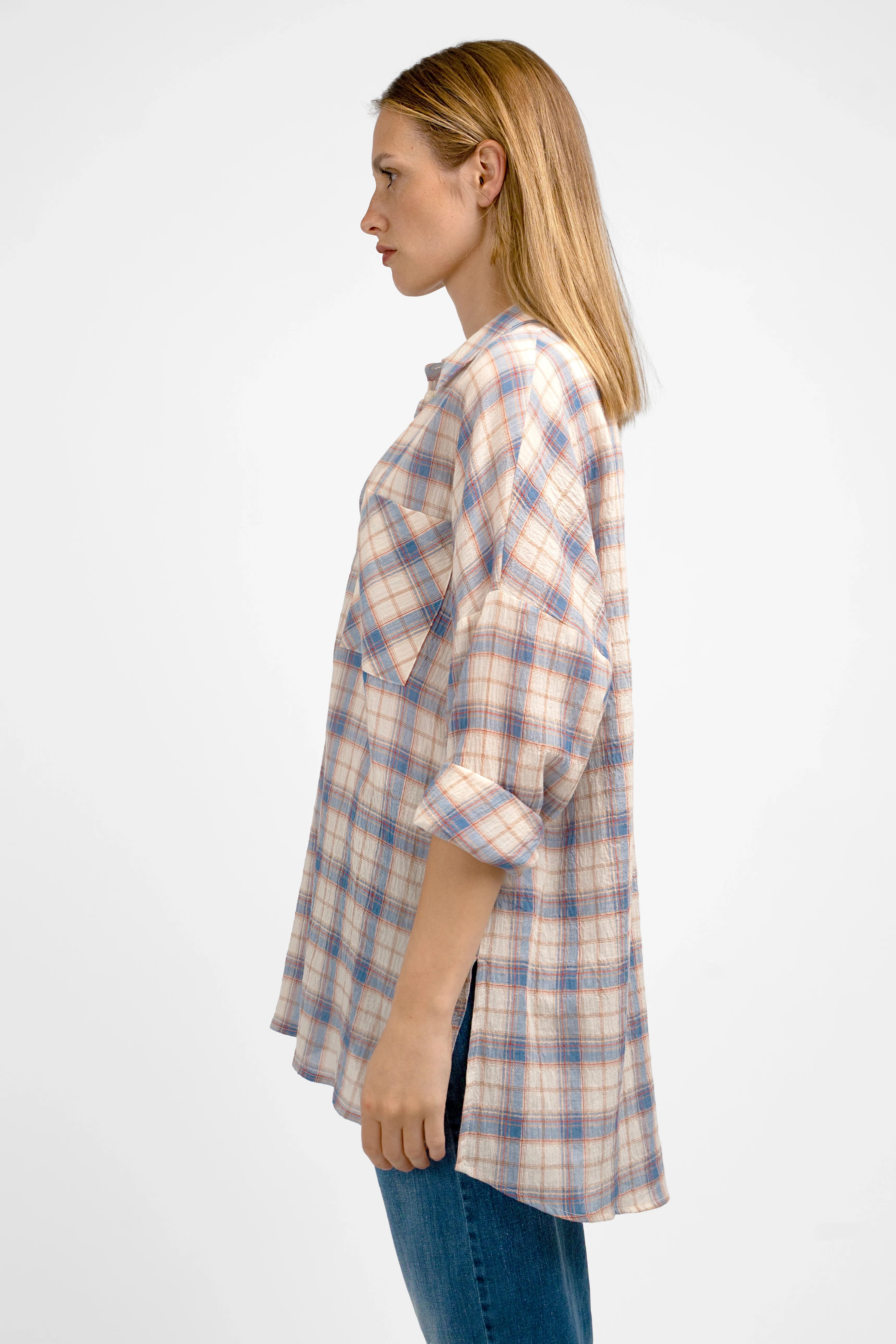 Side view of a woman wearing a relaxed fit ATLE Hemd with crinkle texture, semi-transparent plaid pattern, dropped shoulders, chest pockets, and rolled-up sleeves