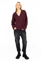 Woman wearing a BERLEY Relaxed V-Neck Bluse in dark burgundy with relaxed fit and V-neckline paired with black jeans and boots
