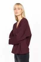 Woman wearing a relaxed fit BERLEY V-neck blouse in dark burgundy made of soft, wrinkle-resistant jersey with dropped shoulders and straight sleeves.
