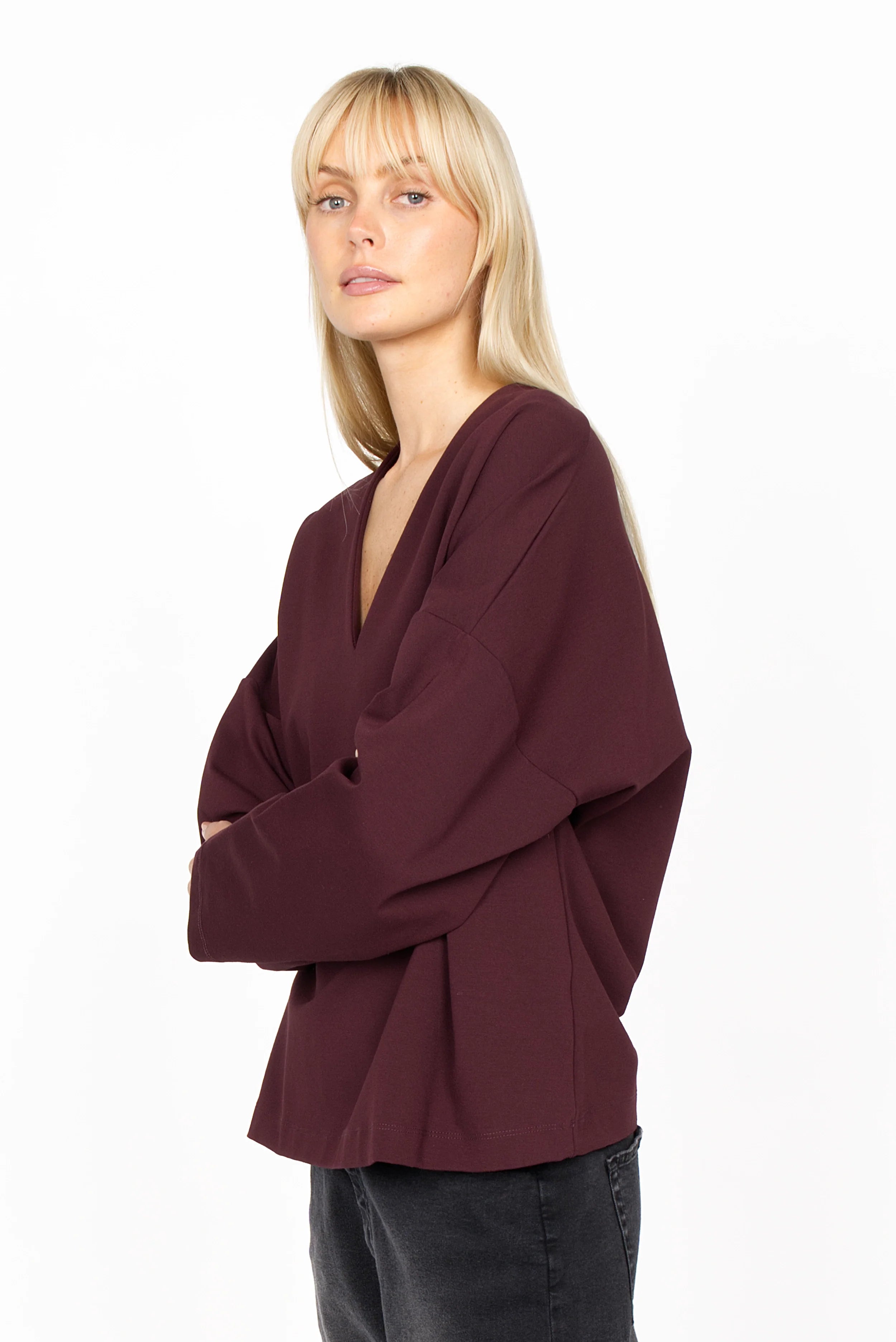 Woman wearing a relaxed fit BERLEY V-neck blouse in dark burgundy made of soft, wrinkle-resistant jersey with dropped shoulders and straight sleeves.