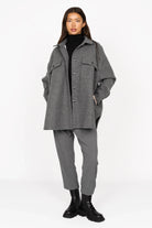 Woman wearing grey BJORA Overshirt with chest pockets and side pockets over black turtleneck and grey pants