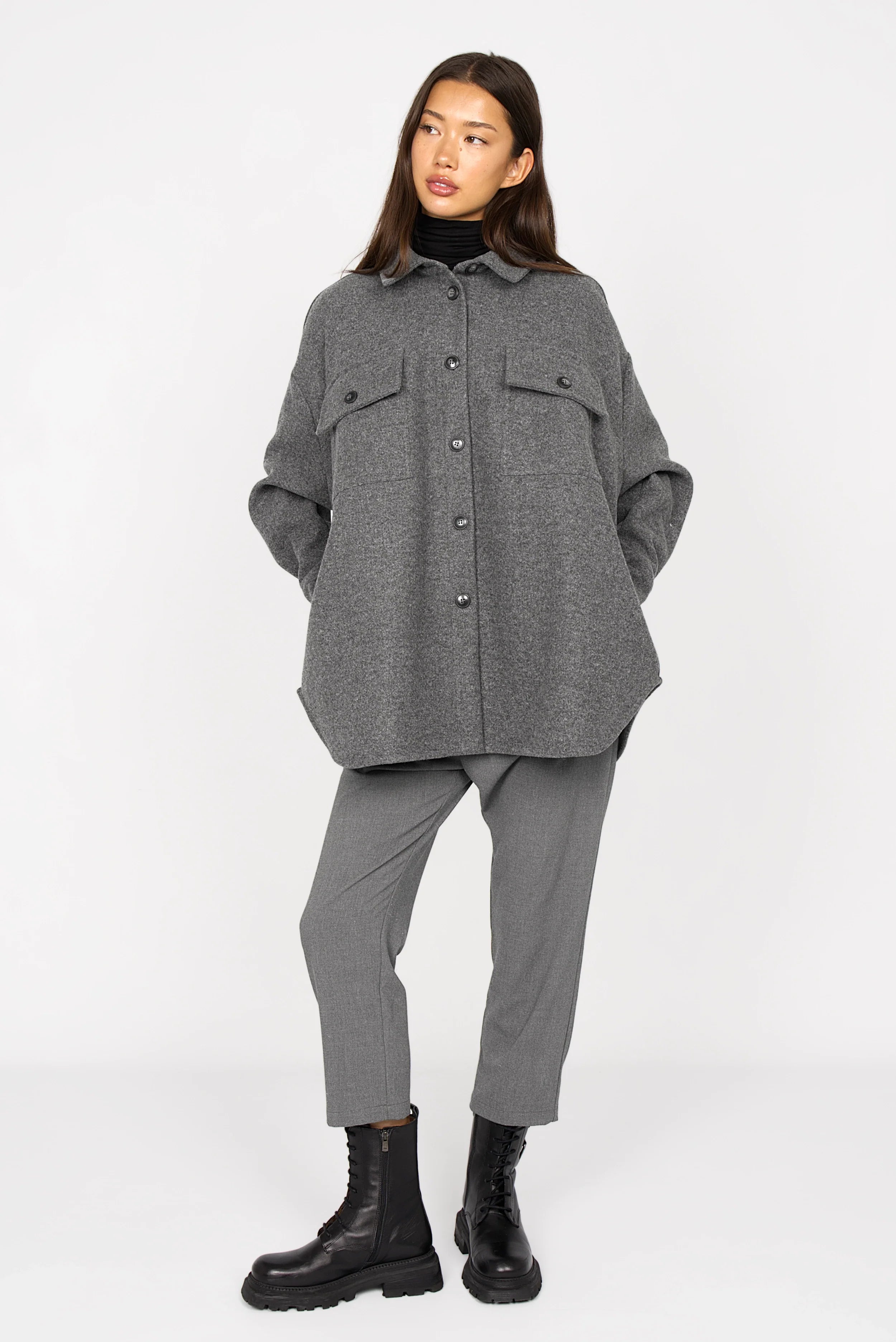 Woman wearing a gray BJORA Overshirt made of wool blend with chest pockets and side pockets, styled with gray pants and black boots.