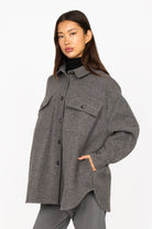 Woman wearing gray BJORA Overshirt made of wool blend with chest and side pockets, button cuffs, and rounded hem.