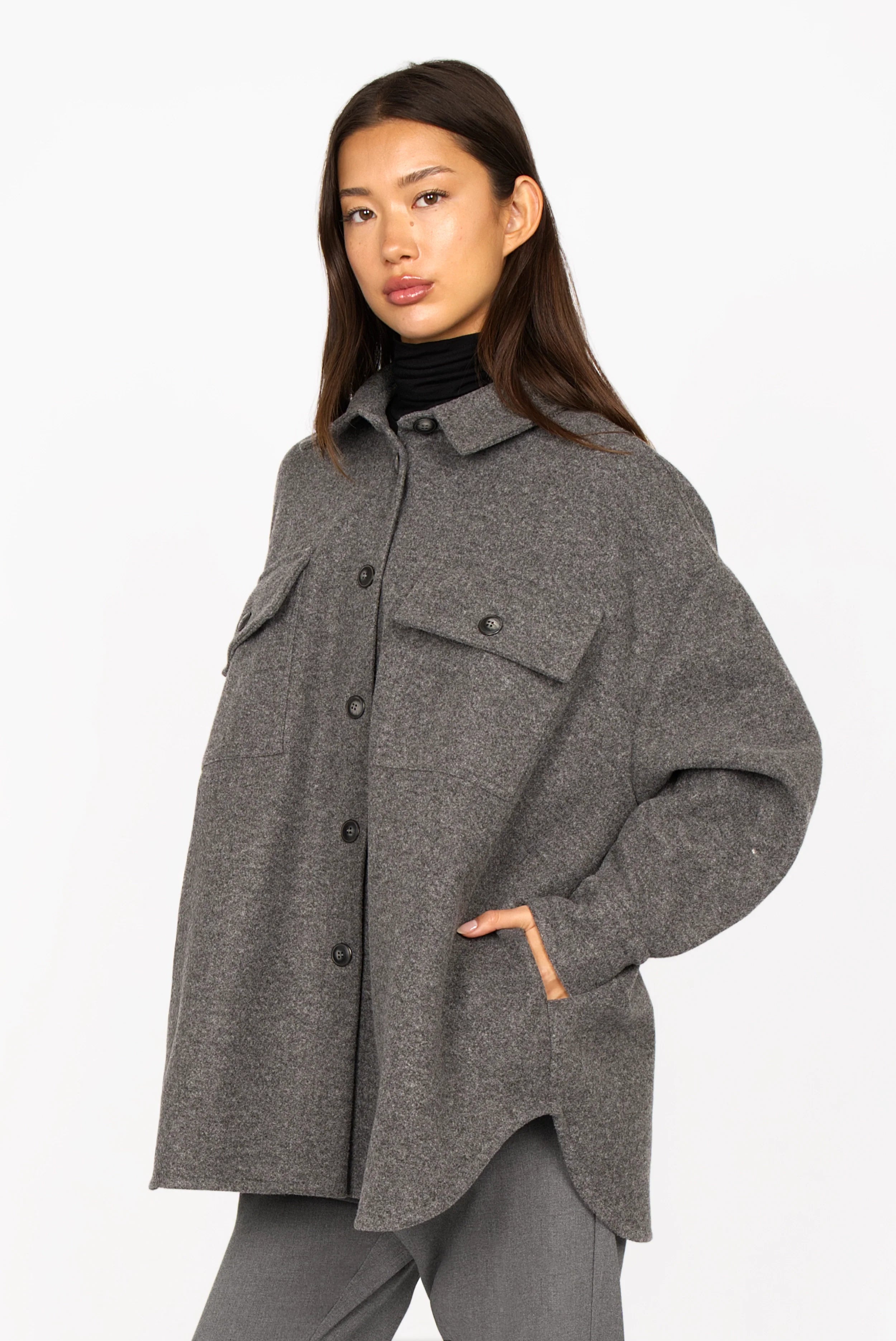 Woman wearing gray BJORA Overshirt made of wool blend with chest and side pockets, button cuffs, and rounded hem.
