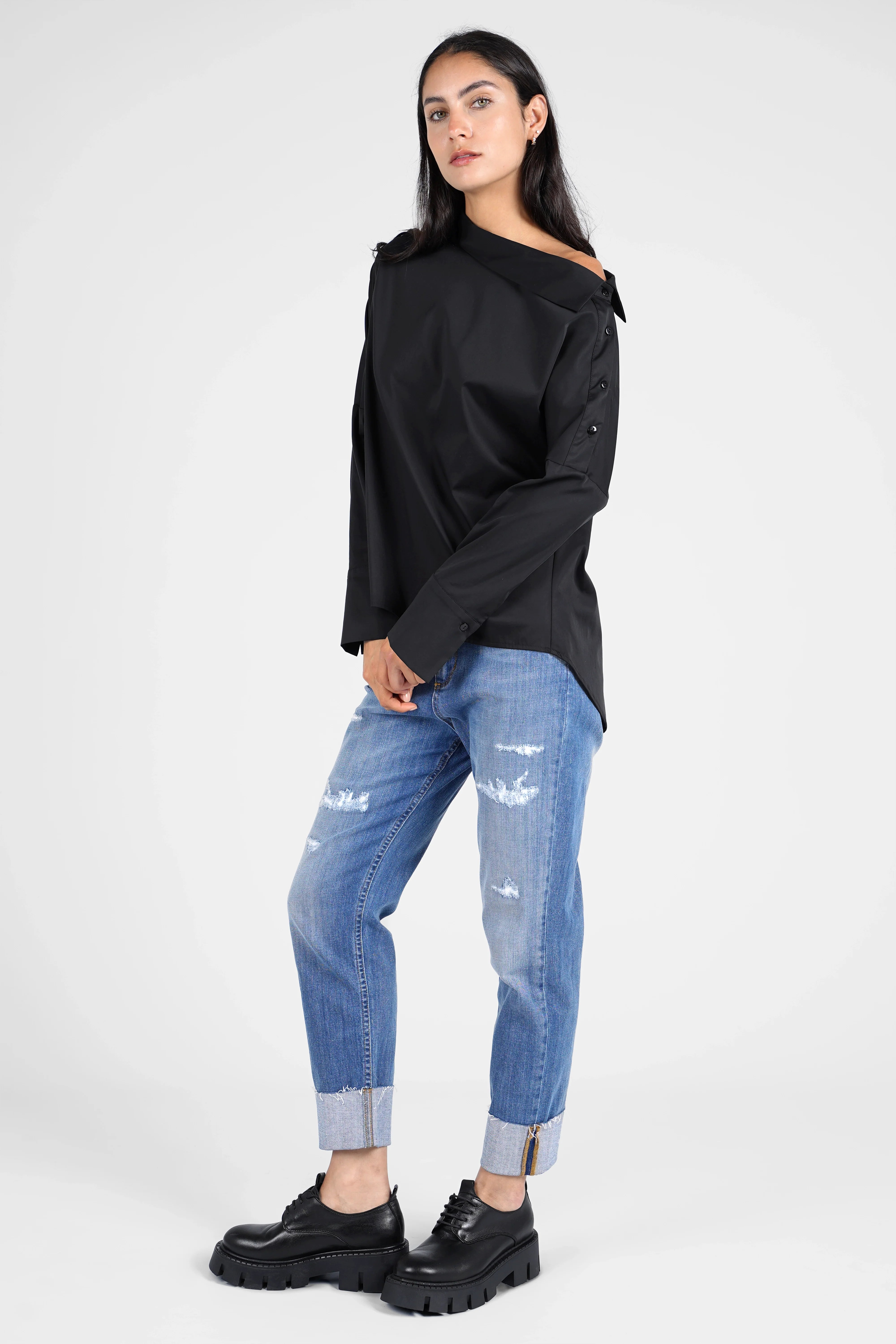 Frau trägt schwarze BONI asymmetrische One Shoulder Bluse mit offenem Schulterknopf und blauer Jeans
