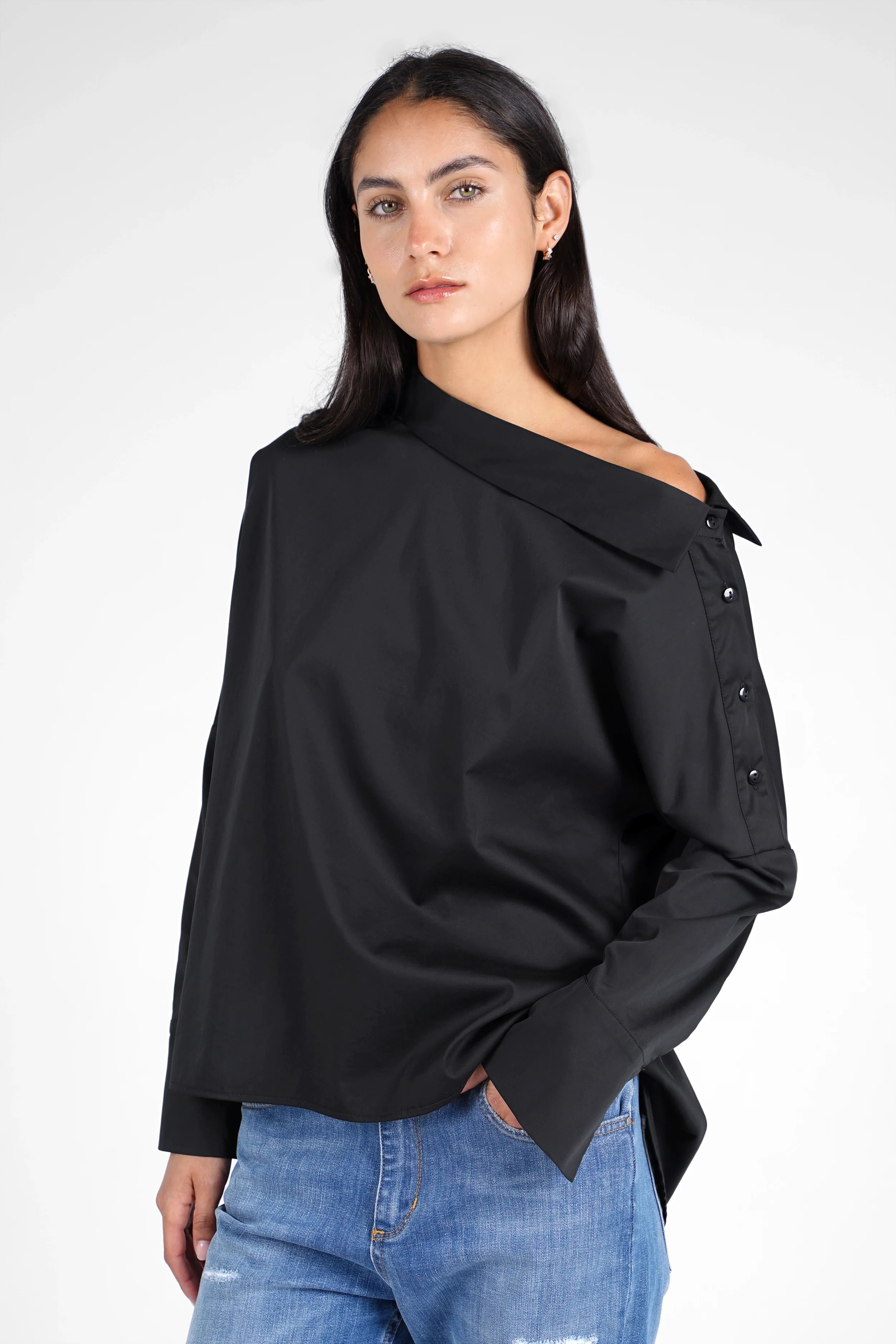 Frau trägt schwarze BONI asymmetrische One Shoulder Bluse mit Knopfleiste und weitem Manschetten, kombiniert mit blauen Jeans
