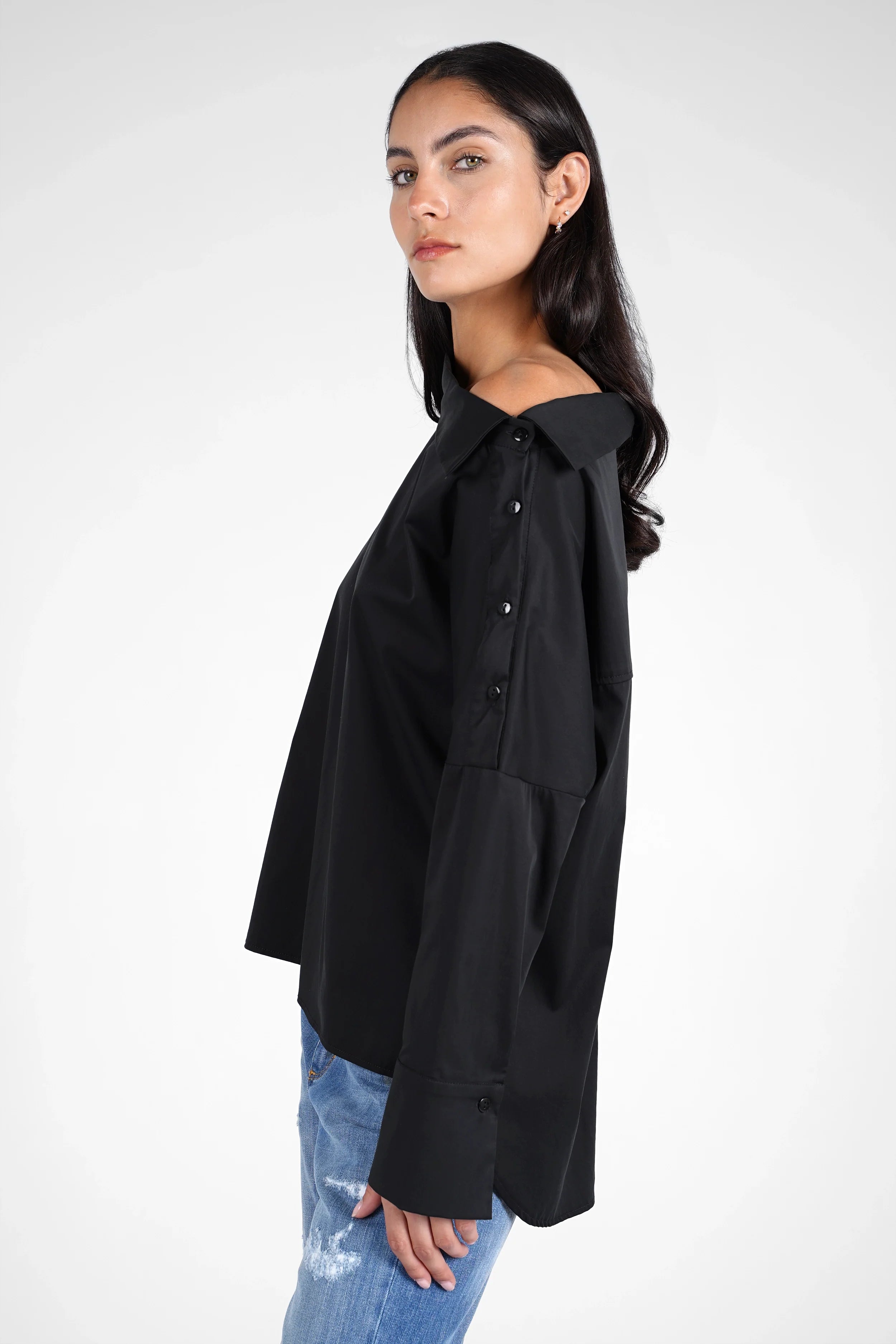 Damen trägt schwarze BONI asymmetrische One Shoulder Bluse mit Knopfleiste und weitem Schnitt zur Jeans