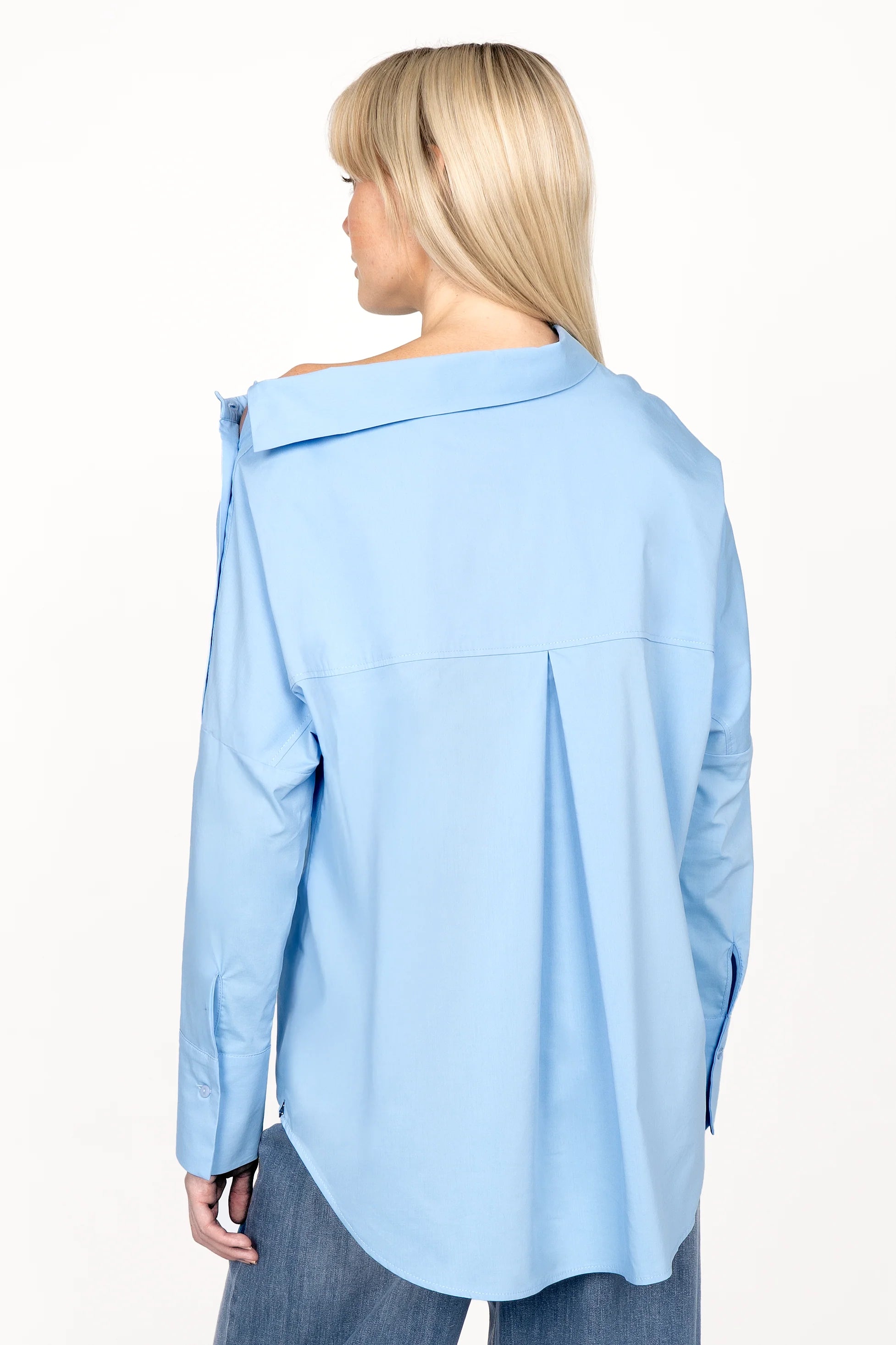 Woman wearing light blue BONI asymmetrical one shoulder blouse with long sleeves and extended back, viewed from behind.