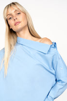 Women wearing BONI asymmetrical one shoulder blue blouse with button details on shoulder and wide cuffs