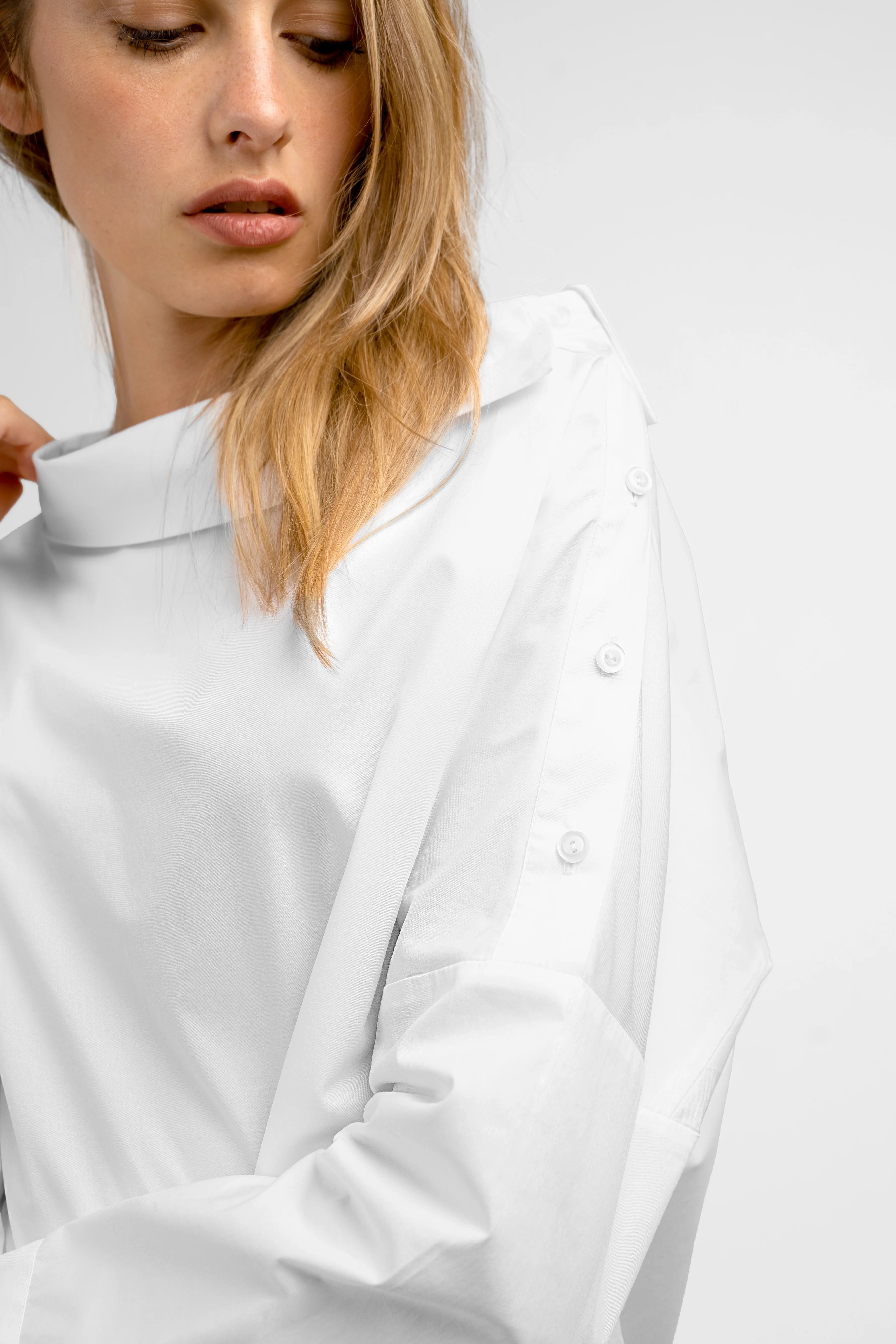 Damen trägt weiße BONI asymmetrische One Shoulder Bluse mit Knopfleiste an der Schulter und breiten Manschetten im relaxed Fit.