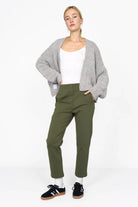 Woman wearing olive green slim fit cropped ankle pants with elastic back waist, paired with white top, gray cardigan, white socks, and black sneakers