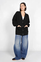 Frau trägt schwarze Relaxed Fit Sweatjacke mit Knopfleiste und aufgesetzten Taschen, kombiniert mit weiten Jeans