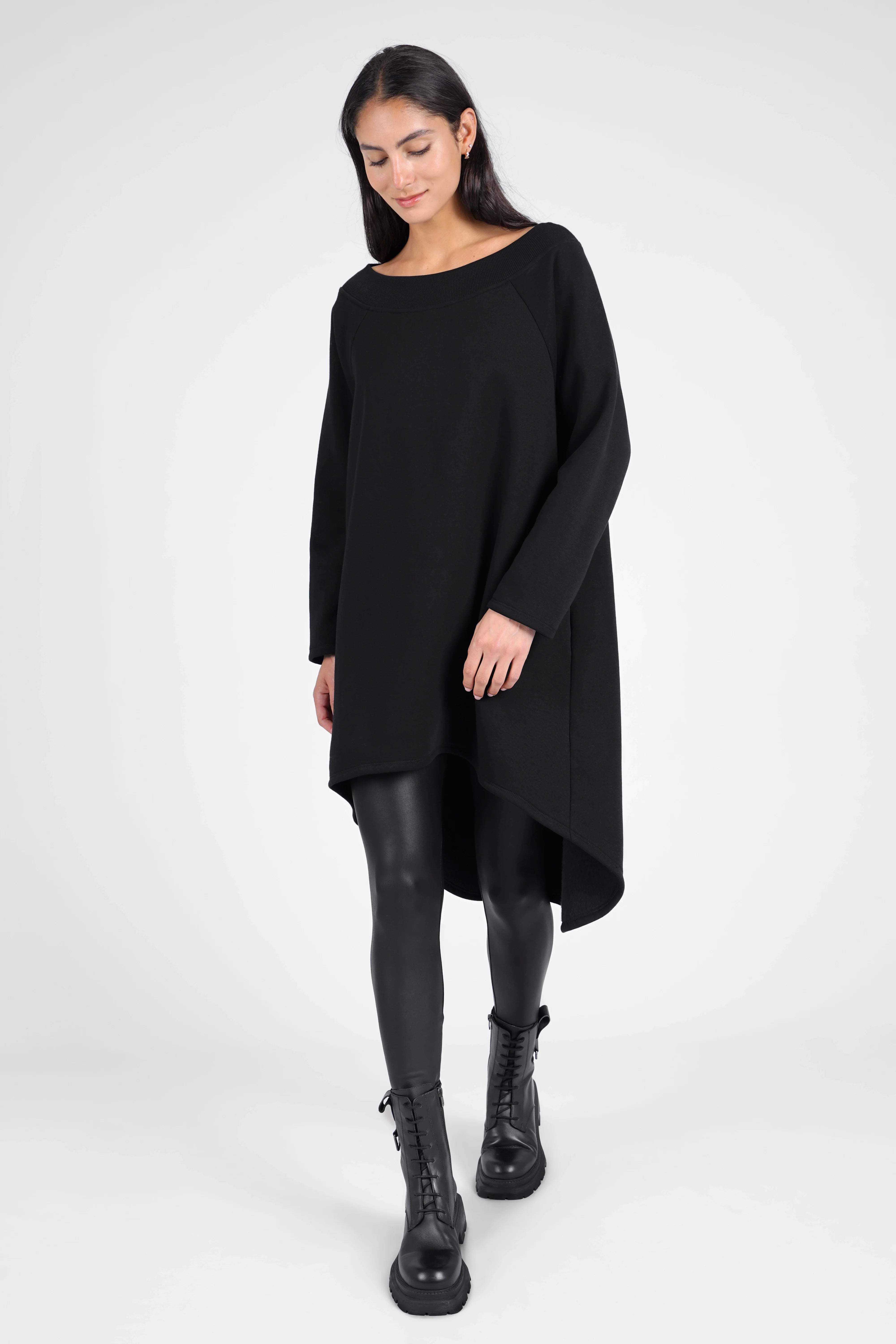 Woman wearing black CHERIN Super-Longsweater with wide boat neckline and asymmetrical hem paired with black leggings and boots