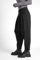 Schwarze DEEP Avantgarde-Hose mit extra tiefem Schritt, seitlicher Knopfschließe, Bundfalten und tapered leg, kombiniert mit soften Materialien und relaxed fit.