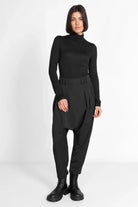 Damenmodell trägt schwarze DEEP Avantgarde-Hose mit extra tiefem Schritt, Bundfalten und seitlicher Knopfleiste in lässigem Relaxed Fit