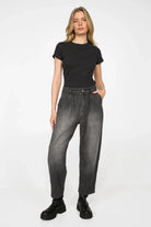 Damenmodell trägt schwarze SAIKA Relaxed Tapered Hose aus strukturierter Baumwolle mit Washed-Effekt und Whisker-Falten, lockere Passform und dezente Karottenform