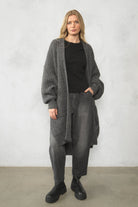 Damen trägt SAIKA Relaxed Tapered Hose aus strukturierter Baumwolle in Washed Black mit lockerer, leicht karottenförmiger Passform und dezenten Whisker-Falten.