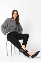 Damen in schwarzen Heelena Tapered Pants mit grauem Pullover, entspannter Slim-Fit-Hose, weichem, knitterarmem Stoff.