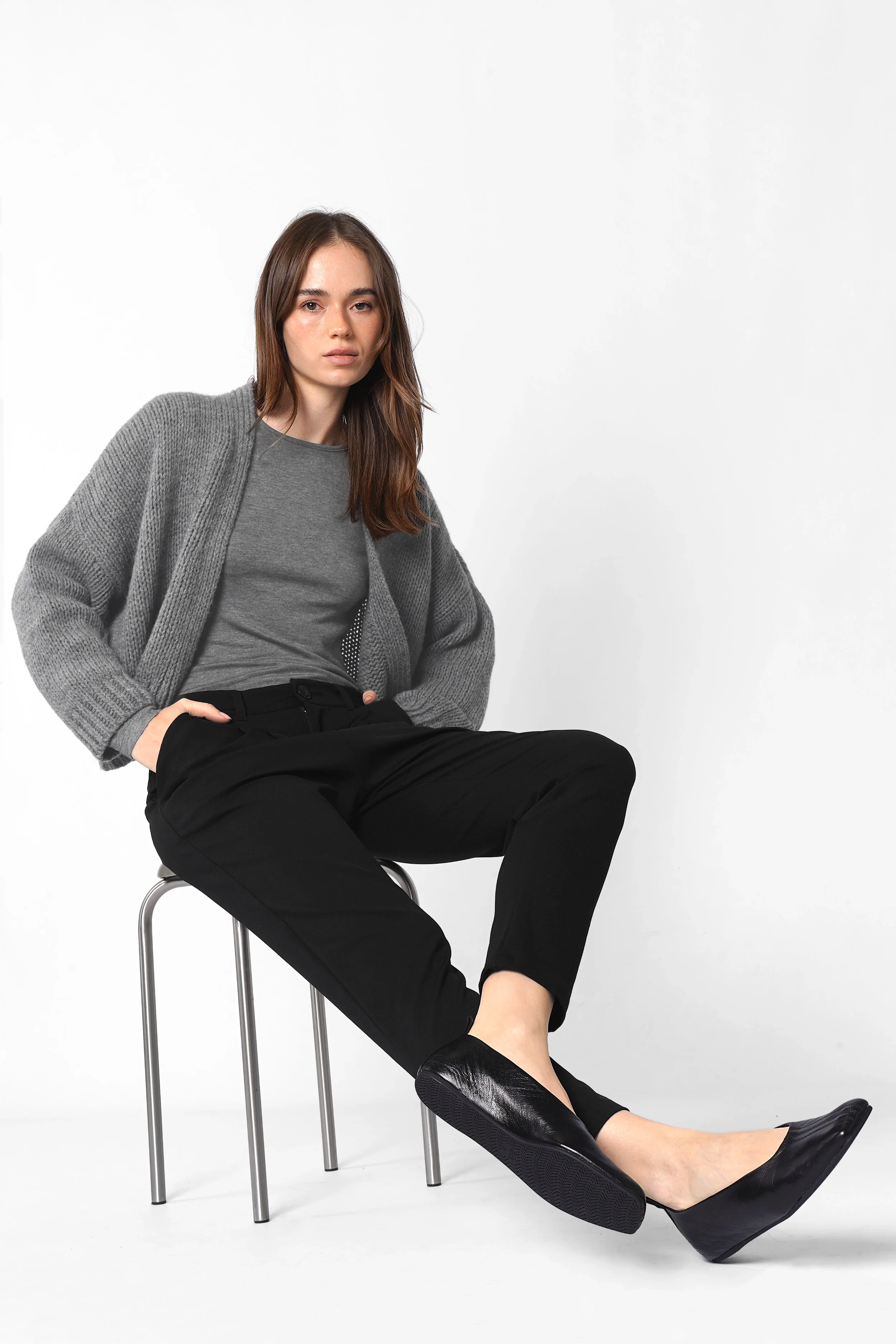 Damen in schwarzen Heelena Tapered Pants mit grauem Pullover, entspannter Slim-Fit-Hose, weichem, knitterarmem Stoff.