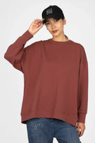 Woman wearing brown EIREL oversize sweater with round neck and dropped shoulders paired with blue jeans and black cap