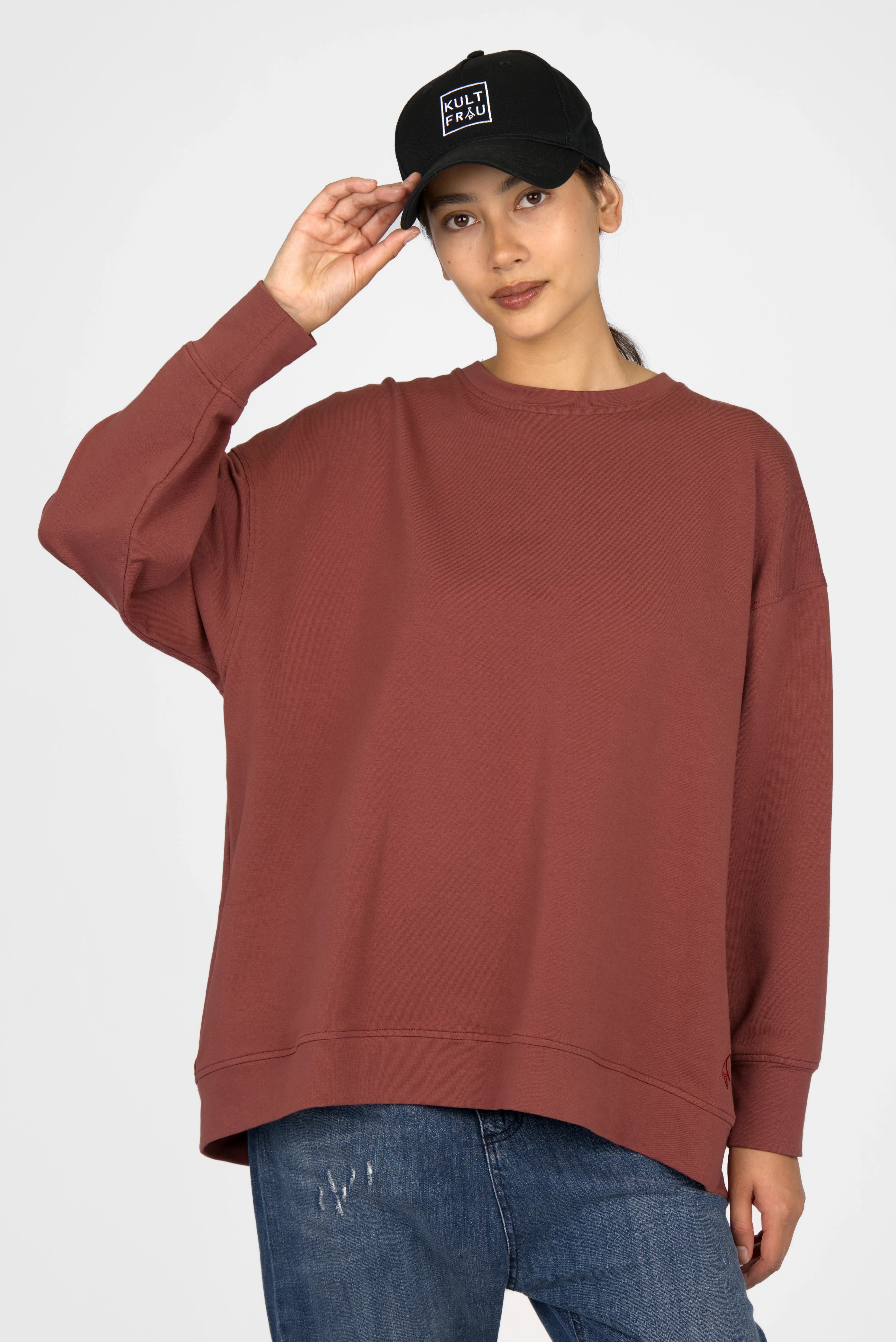 Woman wearing brown EIREL oversize sweater with round neck and dropped shoulders paired with blue jeans and black cap