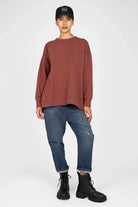 Woman wearing a brown EIREL oversize sweater with round neckline, dropped shoulders, and cuffed sleeves paired with distressed jeans and black boots.