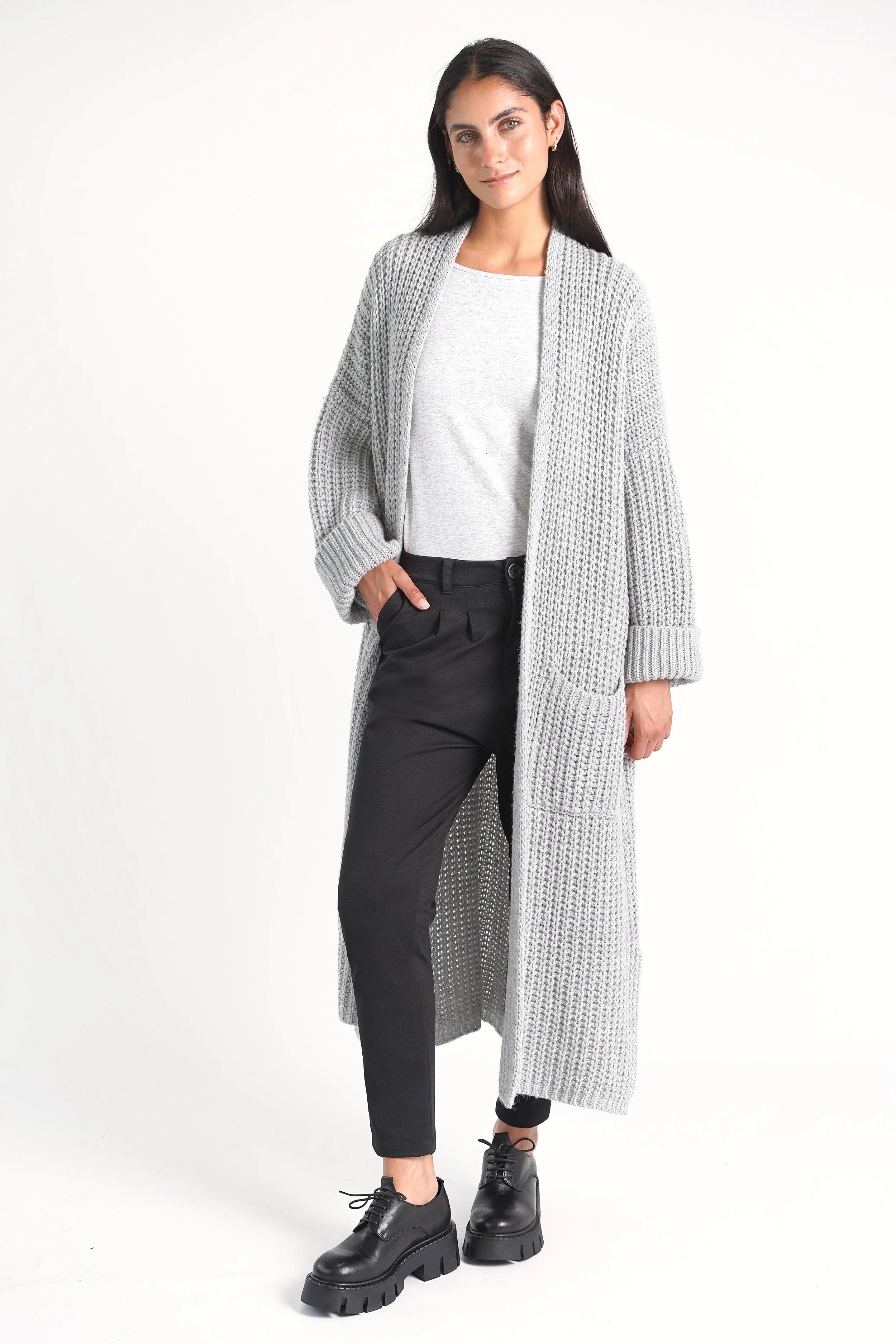 Damenmodel trägt schwarze Heelena Tapered Pants mit modernem, schmal zulaufendem Bein und grauem Strickmantel