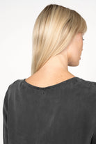 Back view of a woman wearing a black EMEDY Longbluse Tunika with a rounded neckline and soft fabric texture.