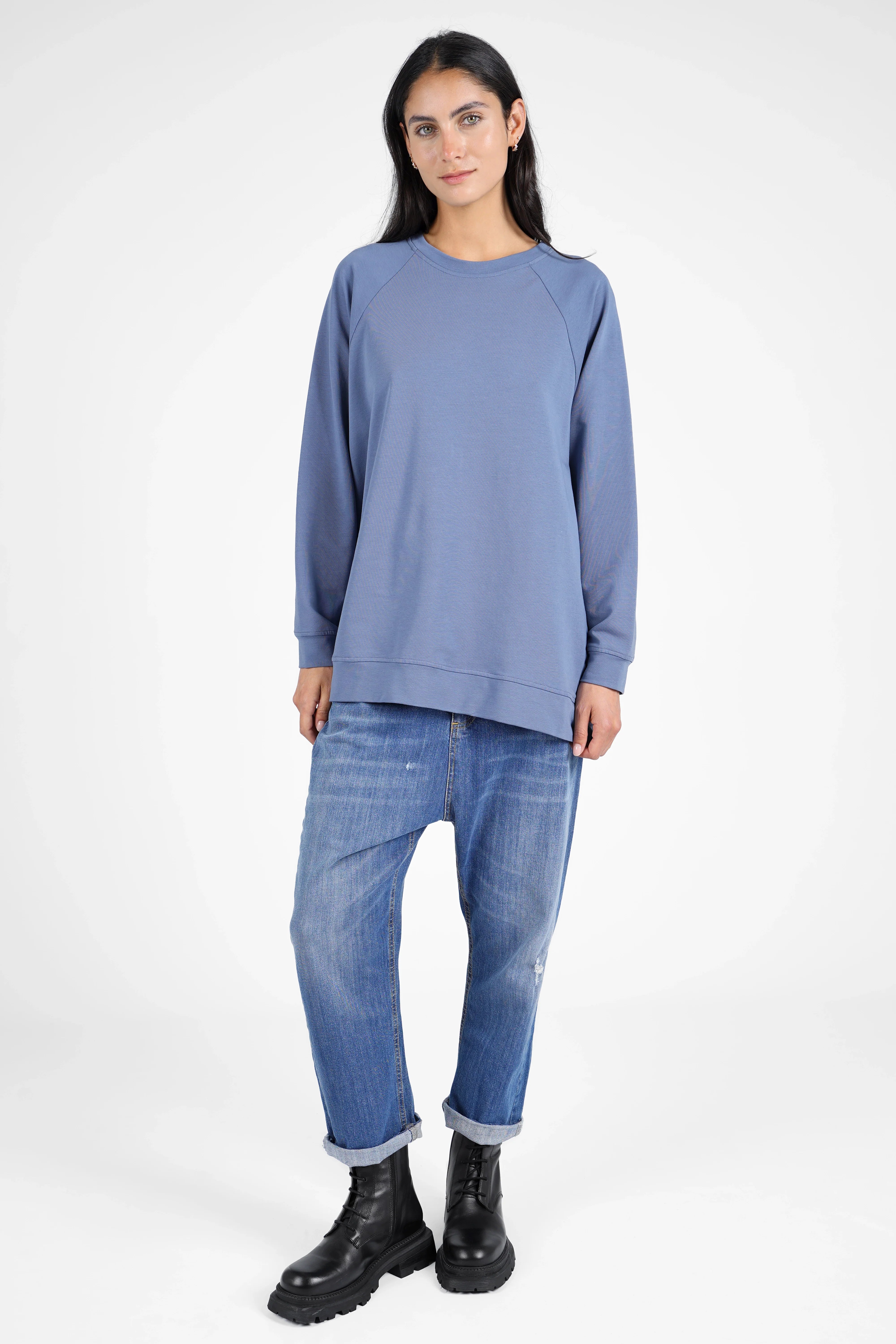 Damen trägt lässigen GRACEY.K Sweater in A-Linie mit Rundhalsausschnitt und Ton-in-Ton Logo-Stickerei, kombiniert mit lässiger Jeans und schwarzen Boots.