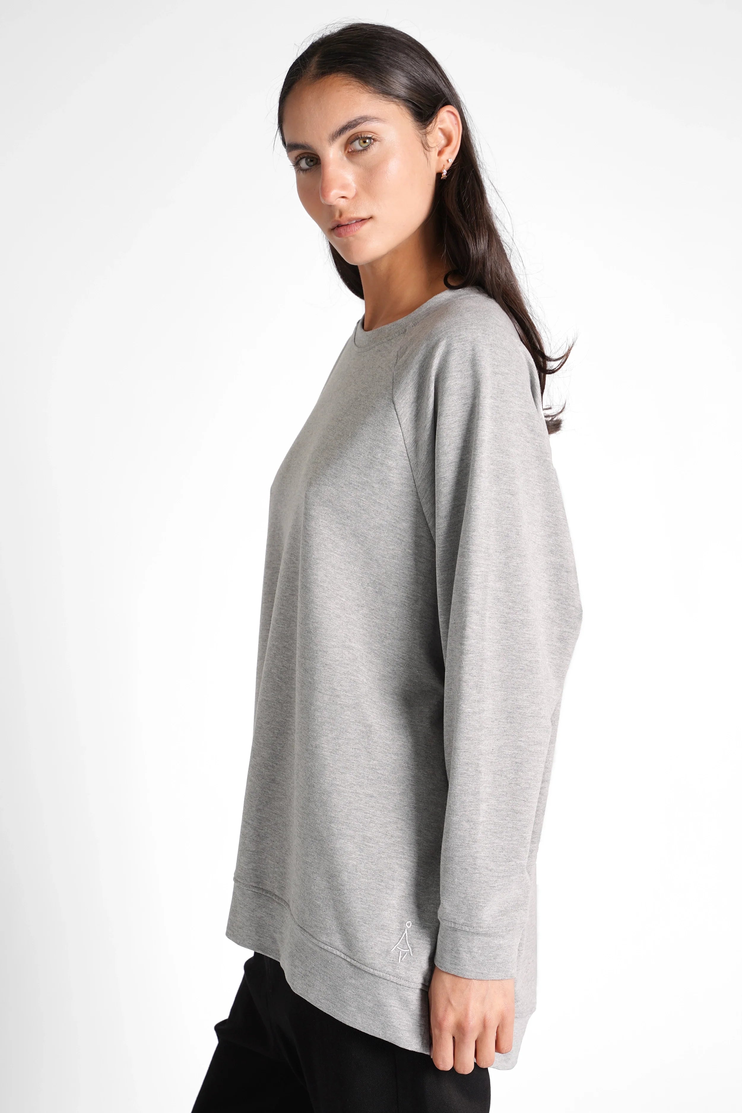 Woman wearing grey oversized GRACEY.K Sweater with rounded hem and tonal logo embroidery, side view.