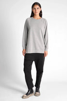 Woman wearing a grey oversized GRACEY.K Sweater with rounded hem and tonal logo embroidery, paired with black pants and black platform shoes.