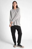Woman wearing a grey GRACEY.K Sweater with round neckline and A-line silhouette paired with black pants and casual shoes.