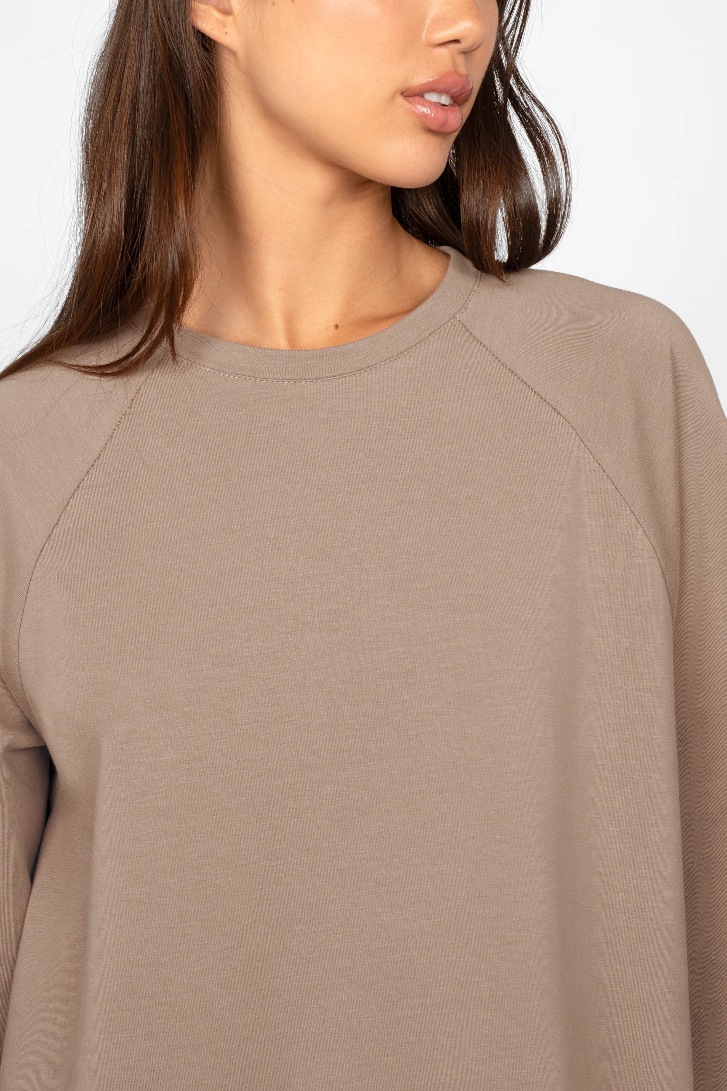 Close-up of a woman wearing a taupe GRACEY.K Sweater with a round neckline, oversize fit, and tonal logo embroidery