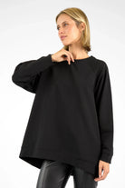 Damen trägt schwarzen oversized GRACEY.K Sweater mit A-Linie und abgerundetem Saum, vorne kürzer, hinten länger geschnitten.