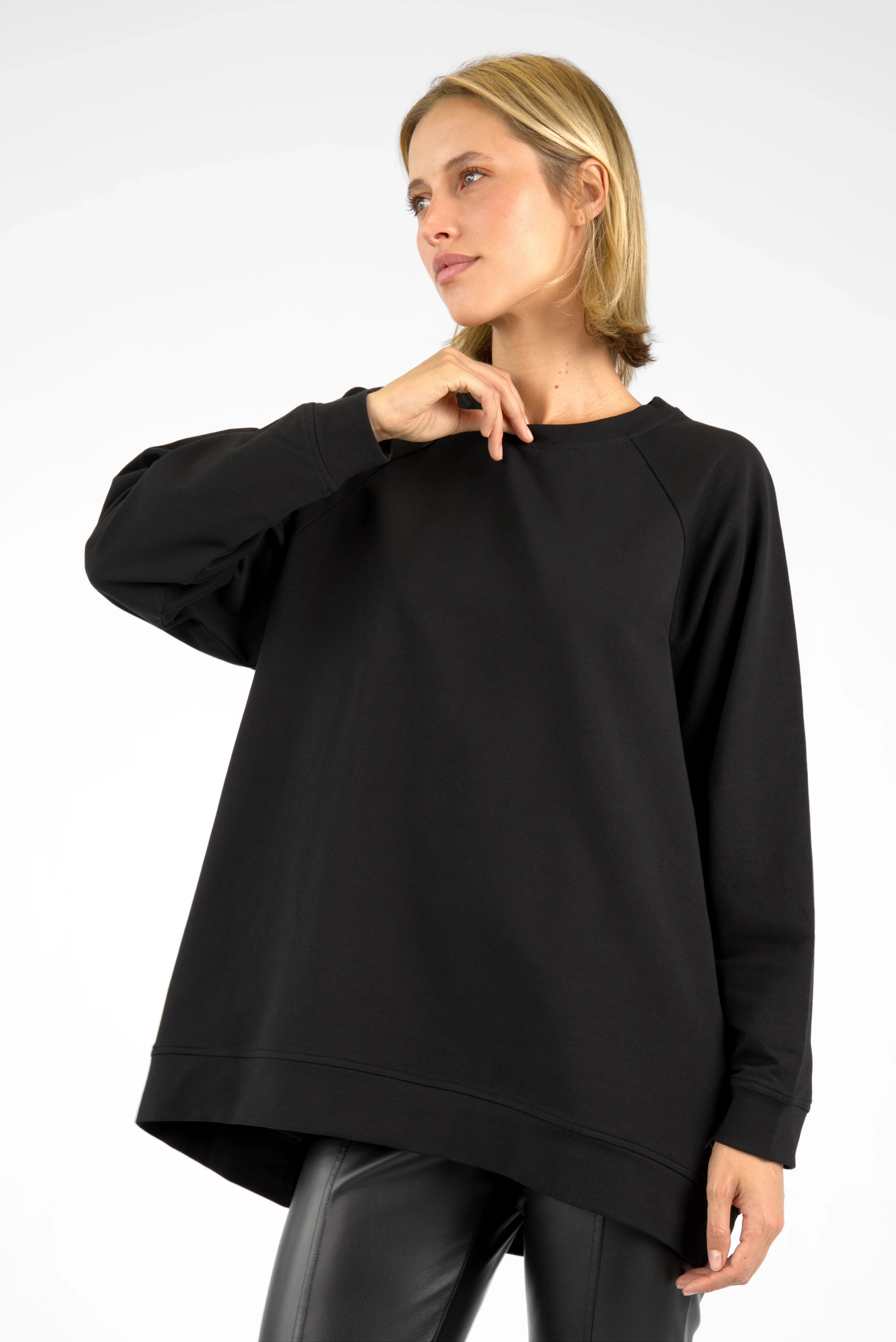 Damen trägt schwarzen oversized GRACEY.K Sweater mit A-Linie und abgerundetem Saum, vorne kürzer, hinten länger geschnitten.