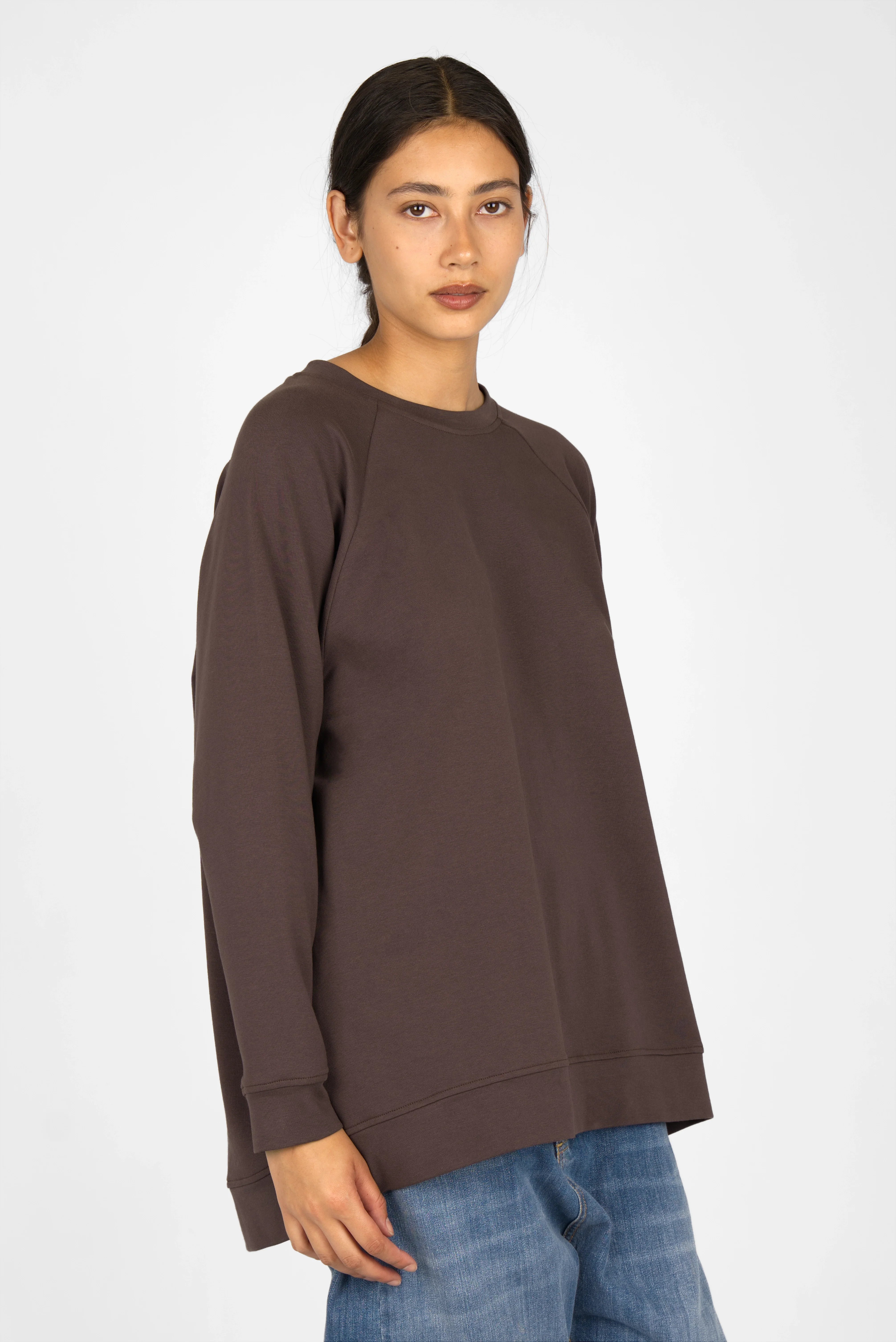 Woman wearing oversized dark brown GRACEY.K Sweater with round neckline and longer back hem paired with blue jeans