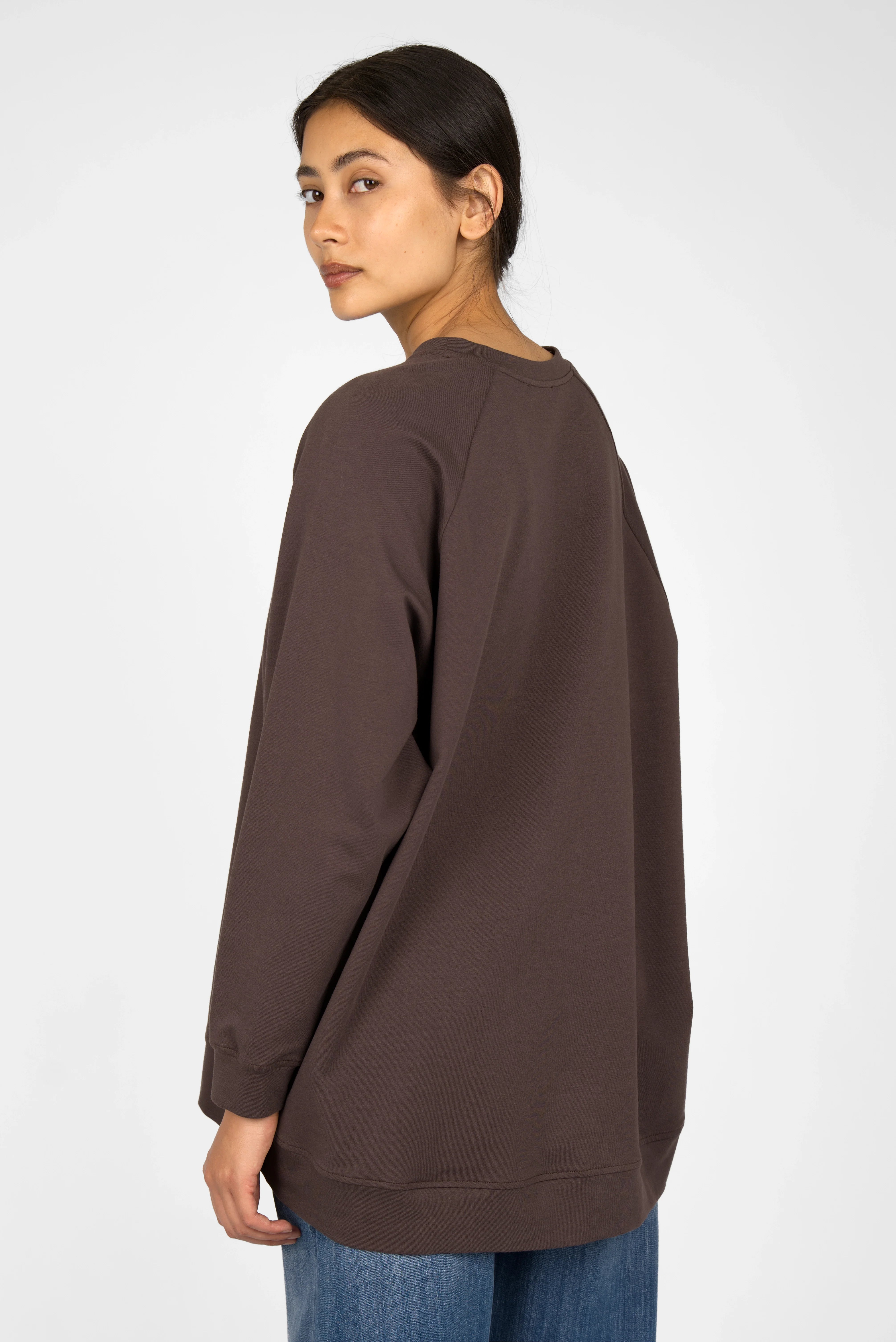 Woman wearing oversized brown GRACEY.K Sweater with rounded hem and tonal logo embroidery, back view.