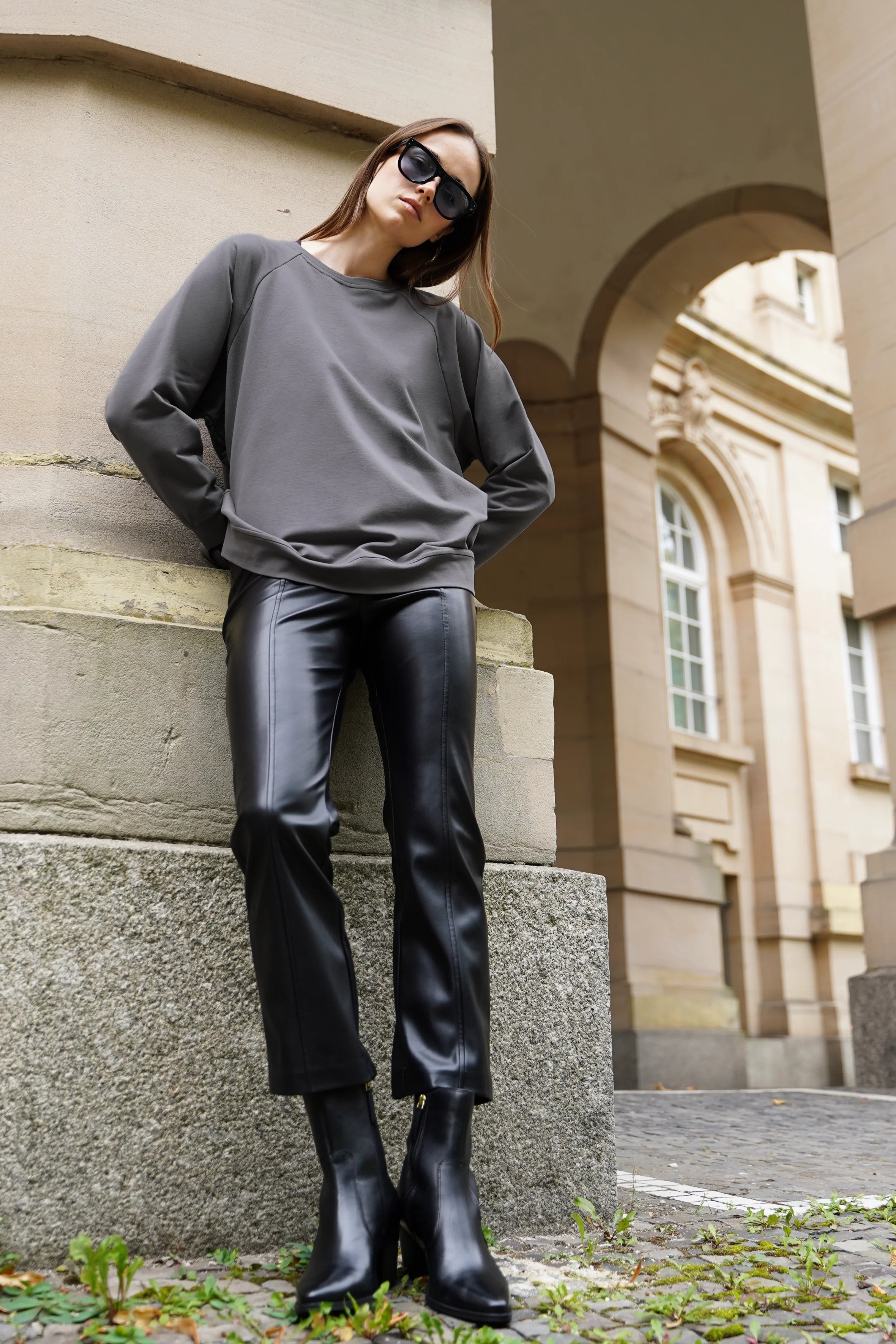 Frau trägt lässigen GRACEY.K Sweater mit A-Linie und tonaler Logo-Stickerei zu schwarzer Lederhose und Sonnenbrille draußen